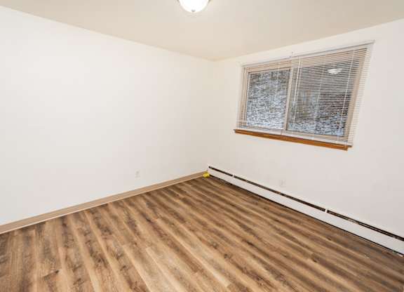 A room with wooden flooring and a window with blinds.