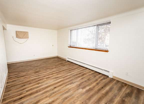 A room with wooden flooring and a window with blinds.