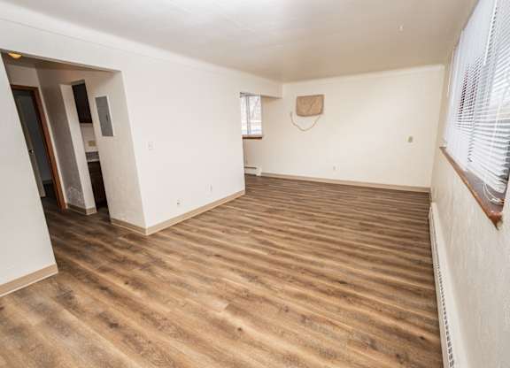 A room with wooden flooring and a window with blinds.
