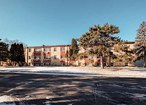A building with a red and beige facade is surrounded by trees and snow.