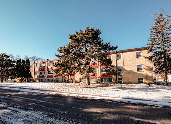 A snowy street with apartment buildings and trees.