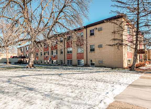Apartment building with snow on the ground and bare trees in front.