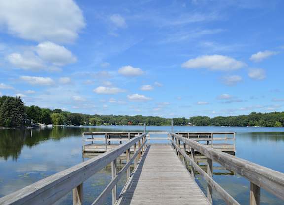 A wooden dock extends into a calm lake with a clear blue sky above.
