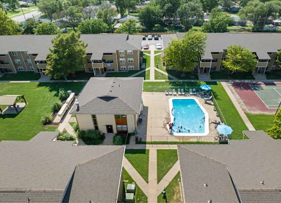 A swimming pool is surrounded by a grassy area and tennis court.