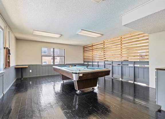 A pool table in a room with wooden floors and a window with blinds.