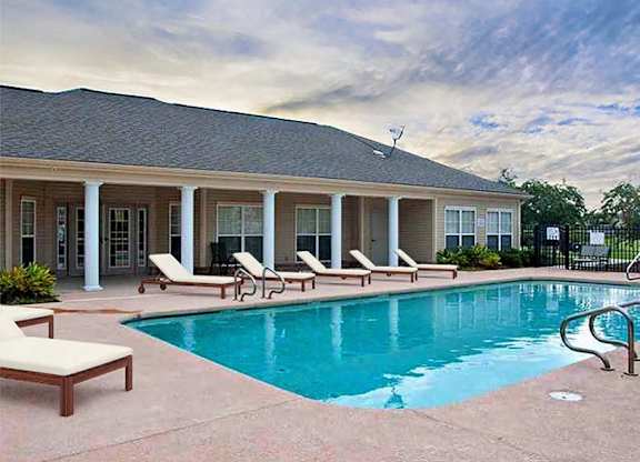 A pool area with sun loungers and a house in the background.
