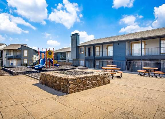 A playground area with a slide, swings, and picnic tables in front of a building.