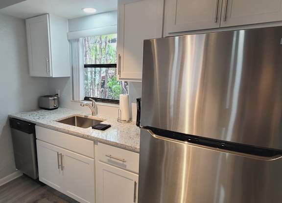 A kitchen with a stainless steel refrigerator and white cabinets.