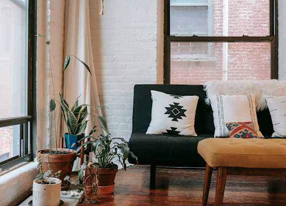 A living room with a black couch, a wooden table, and several potted plants.