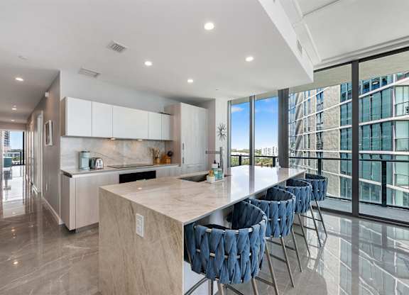 A modern kitchen with a marble countertop and blue chairs.