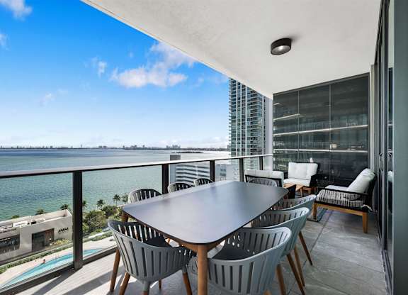 A table with chairs is set up on a balcony overlooking the ocean.