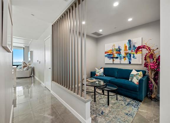 A modern living room with a blue couch and a large abstract painting on the wall.