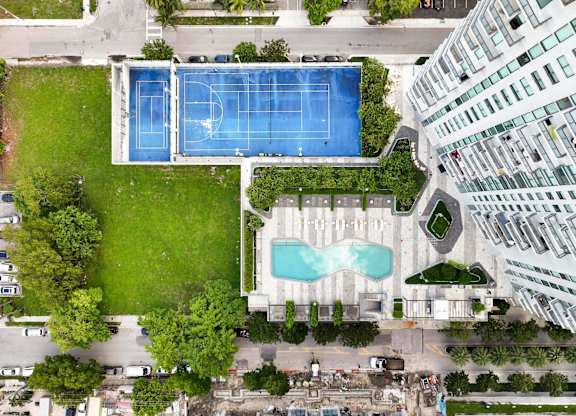 A large swimming pool is surrounded by a grassy area and a tennis court.