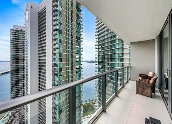 A balcony with a chair and a table overlooks a body of water.