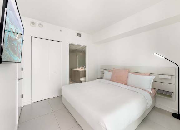 A white bedroom with a bed, nightstand, and a television.