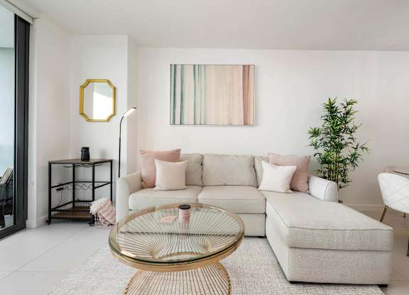 A living room with a white couch, a glass coffee table, and a plant.