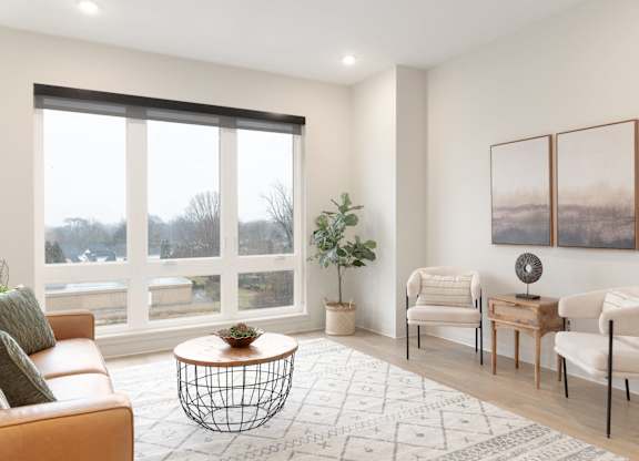 A living room with a large window, a sofa, a coffee table, and two chairs.
