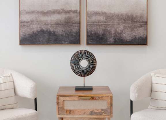 Two framed pictures hang on a wall above a fan and a table.