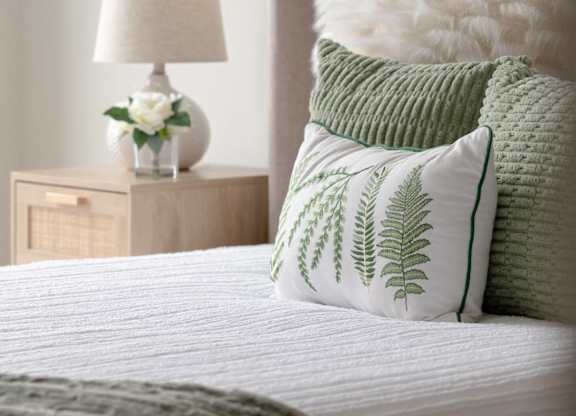 A bed with a white comforter and green pillows with a white lamp on a nightstand.