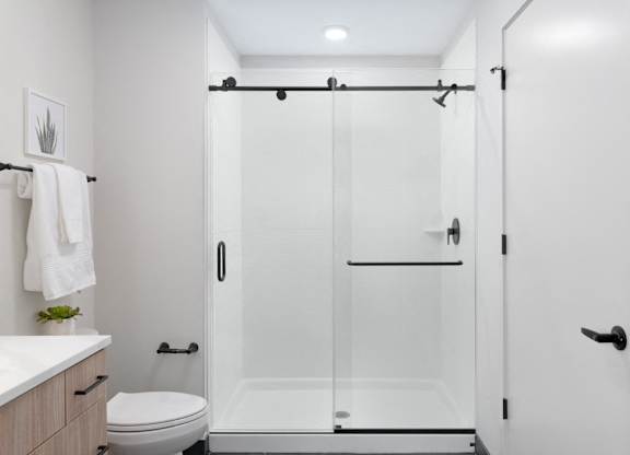 A white bathroom with a toilet, sink, and a walk-in shower.