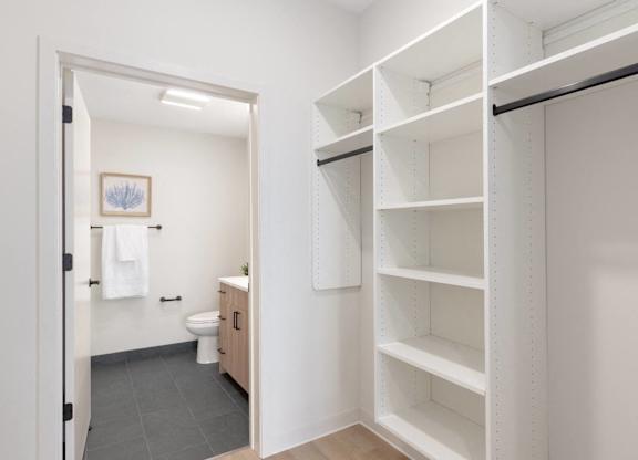A white bathroom with a toilet and a white closet with shelves.