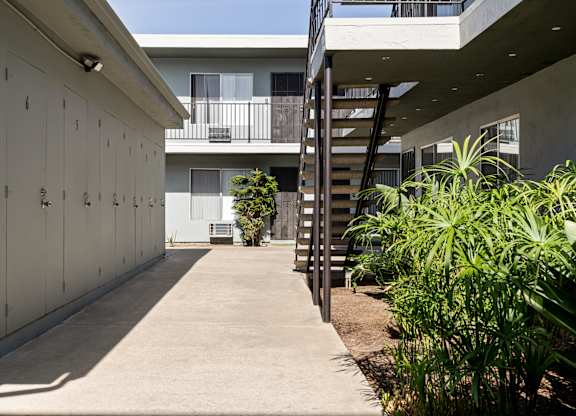 A concrete pathway leads to a building with a balcony and a staircase.