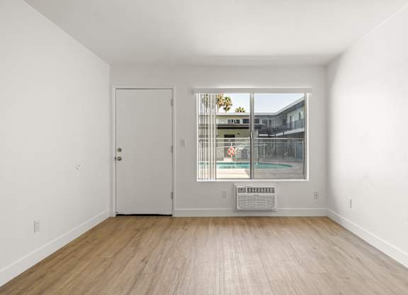 A room with a white door and a window with a view of a building.
