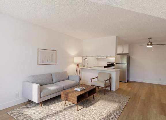 A living room with a grey couch, a wooden coffee table, and a white kitchen area in the background.