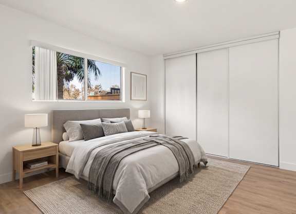 A bedroom with a large bed and a window showing a view of a palm tree.
