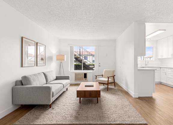 A living room with a grey sofa, a wooden coffee table, and a kitchen area with a refrigerator.