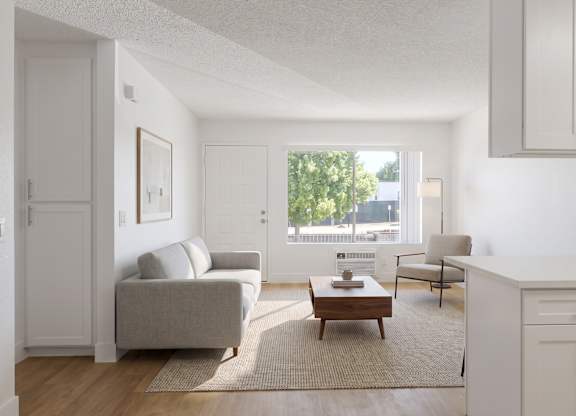 A living room with a grey couch, a coffee table, and a window with a view of trees and buildings outside.