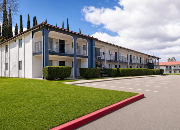 A row of white and blue buildings with balconies and a red stripe along the grass.
