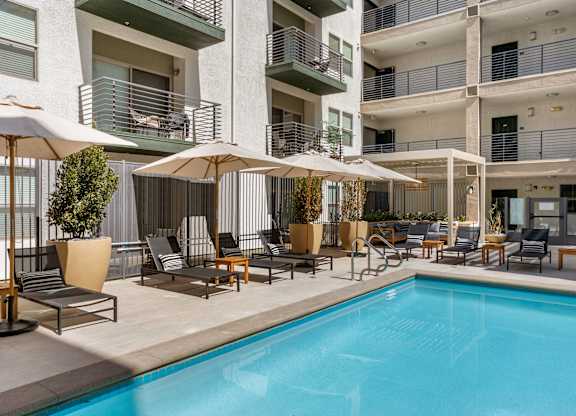 A pool area with chairs and umbrellas in front of a building.