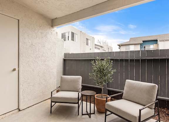 Two chairs and a table are on a balcony.