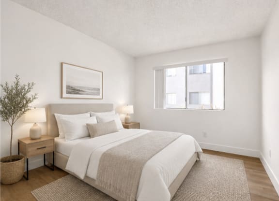 A bedroom with a large bed, a nightstand with a lamp, and a framed picture on the wall.
