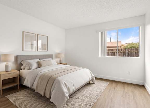 A bedroom with a large bed and a window overlooking a fence.