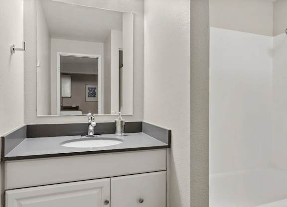 A bathroom with a sink, mirror, and shower.