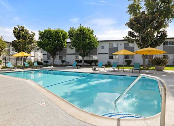 A swimming pool surrounded by trees and chairs with umbrellas.
