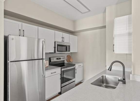 A kitchen with a refrigerator, oven, sink, and microwave.