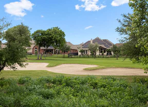 A view of a green field with trees and a building in the background.