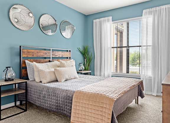 A bedroom with a bed, nightstand, and window with white curtains.