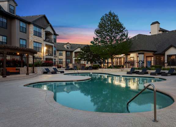 A large outdoor swimming pool surrounded by lounge chairs and buildings.
