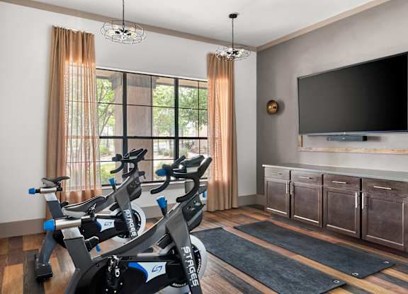 A room with a television, a window with curtains, and a row of exercise bikes.