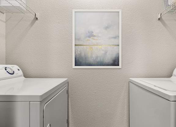 A laundry room with a washing machine and a painting on the wall.