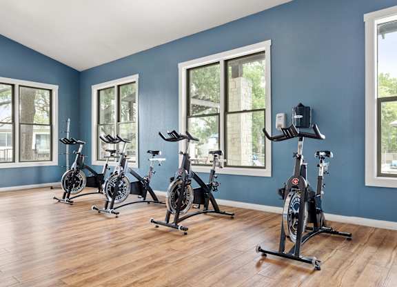 A room with blue walls and wooden floors has exercise bikes in it.