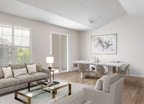 A modern living room with a grey sofa, a glass coffee table, and a dining table set up.