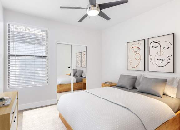A bedroom with a bed, a nightstand, a window with blinds, a ceiling fan, and two framed artworks on the wall.