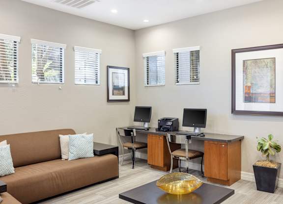 A living room with a brown couch, a desk with a computer, and a framed picture on the wall.