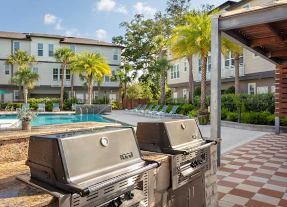Two grills are in the foreground of a resort with a pool and palm trees.