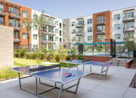 A ping pong table is in the middle of a courtyard with apartment buildings in the background.